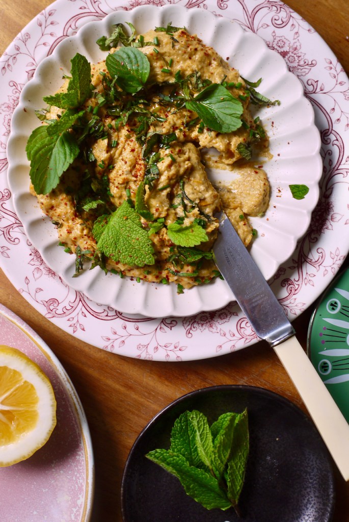 A plate of dip with mint leaves and a knife resting on it.