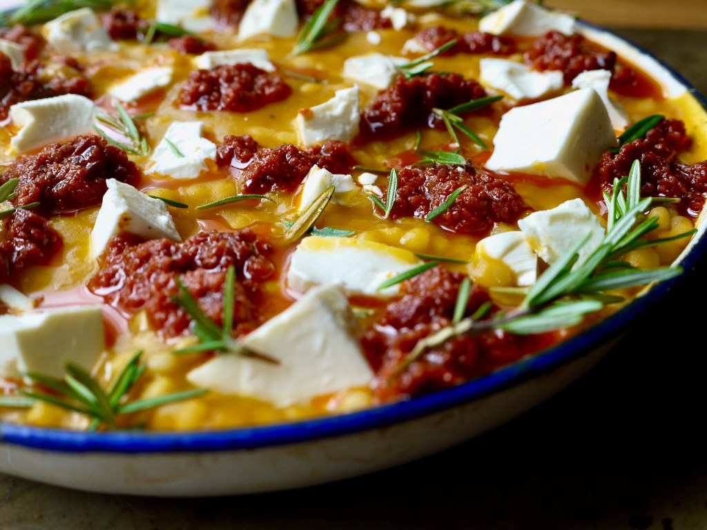 A close up of a dish with cubes of feta and rosemary leaves.